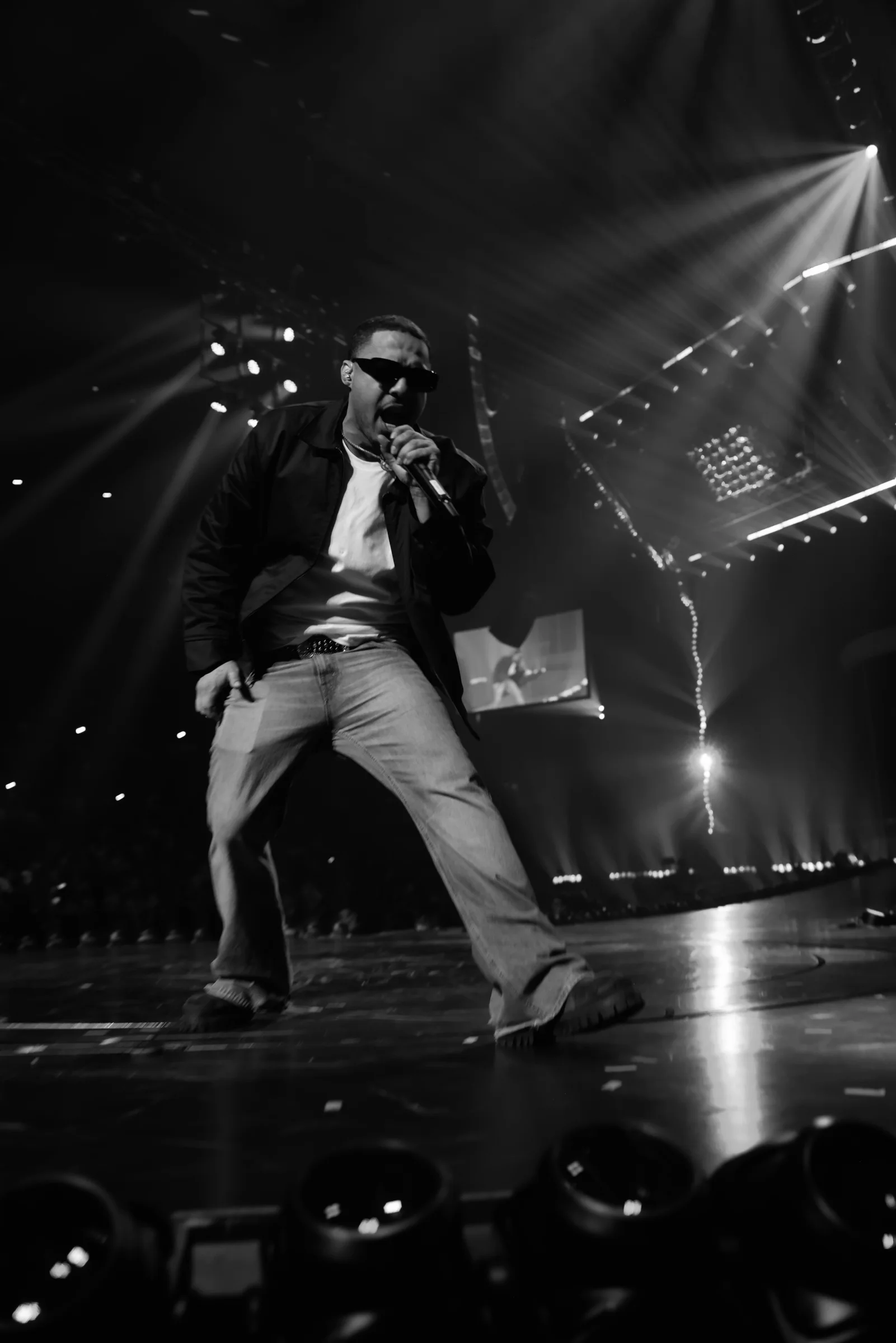 DJ Ray G commanding the stage with a microphone beneath concert lights.